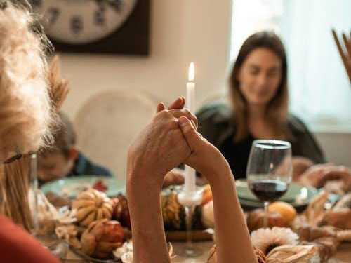 People holding hands around a dinner table with a lit candle icon