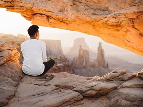 A person sitting in a a rock formation looking out into the distance icon